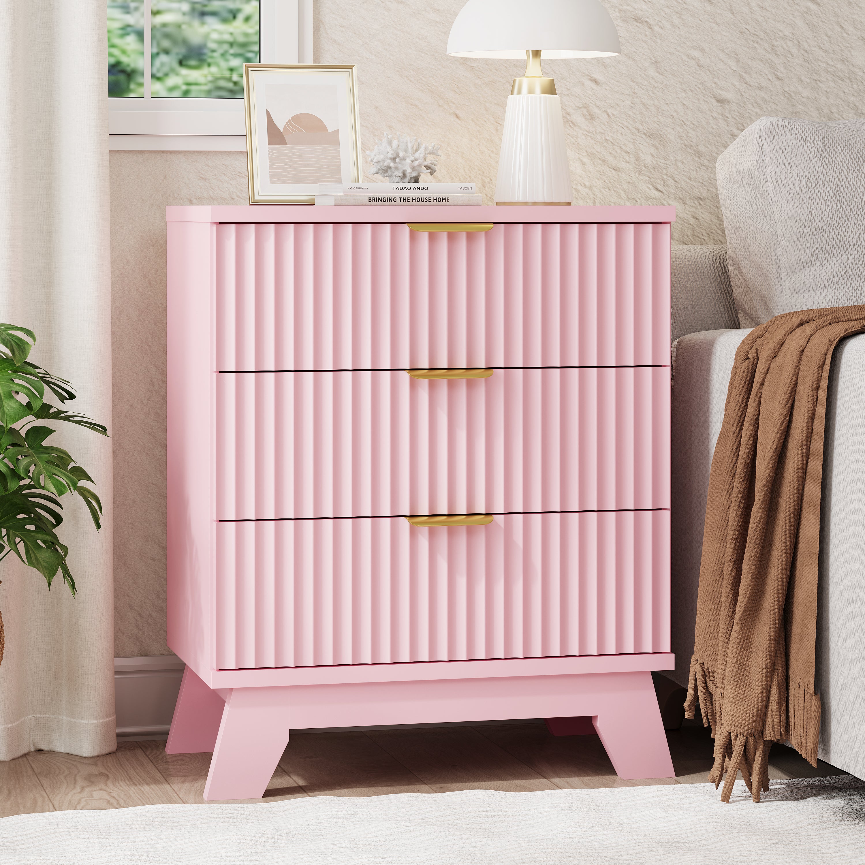 Linea modern pink fluted 3-drawer nightstand with gold metal handles, styled with a white lamp and framed art by a window.