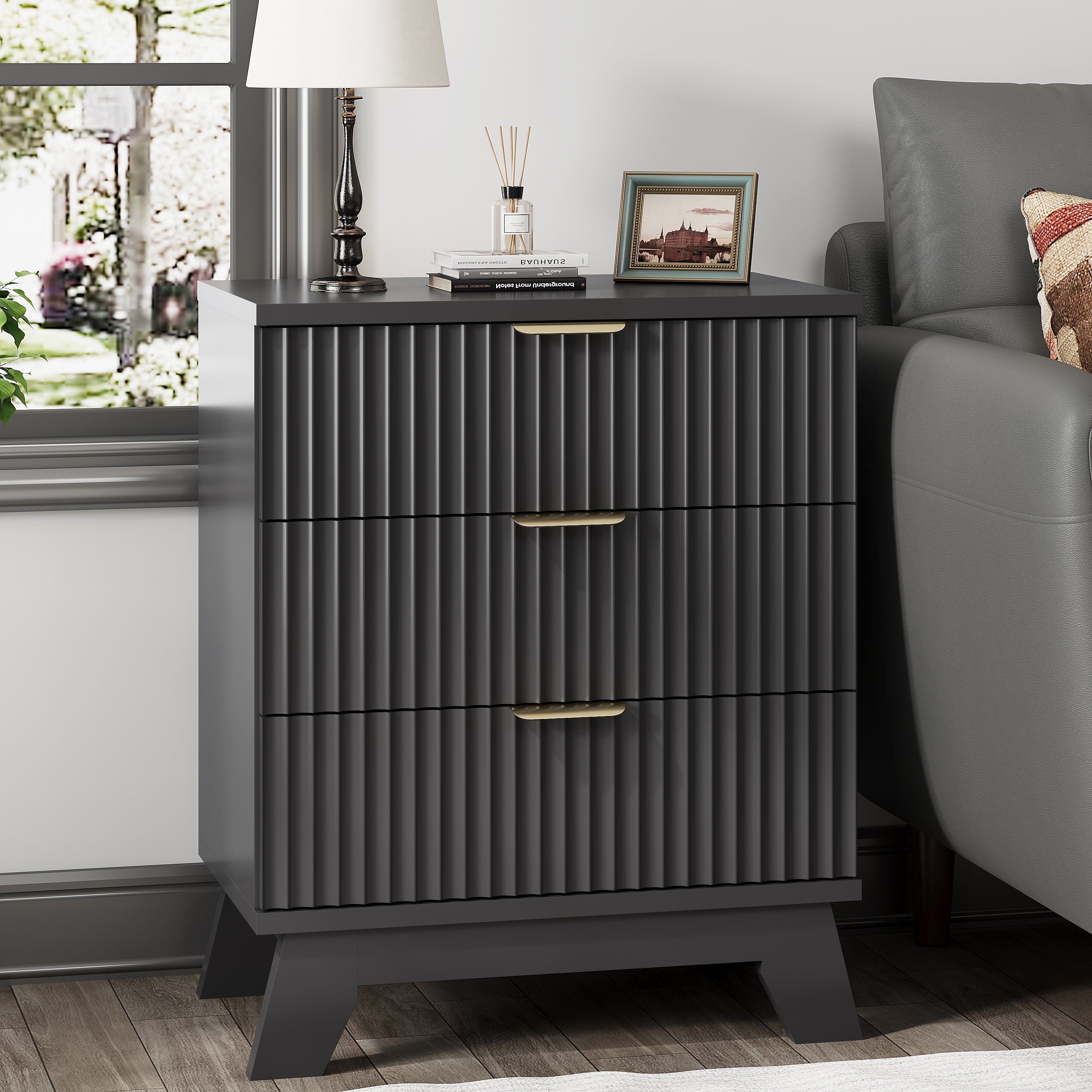 Linea modern black fluted 3-drawer nightstand with gold metal handles, styled with a white lamp and framed art by a window.