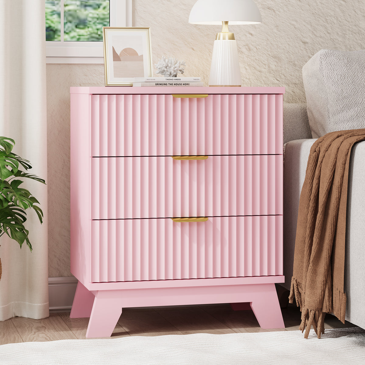 Linea modern pink fluted 3-drawer nightstand with gold metal handles, styled with a white lamp and framed art by a window.